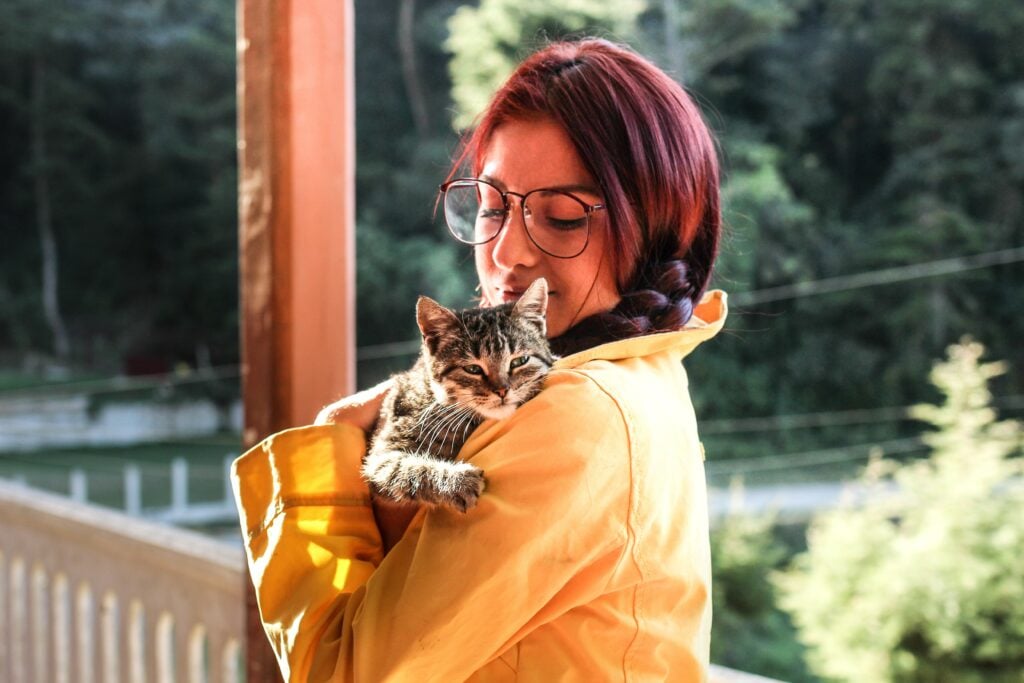 Woman holding cat looking over her shoulder on a porch.